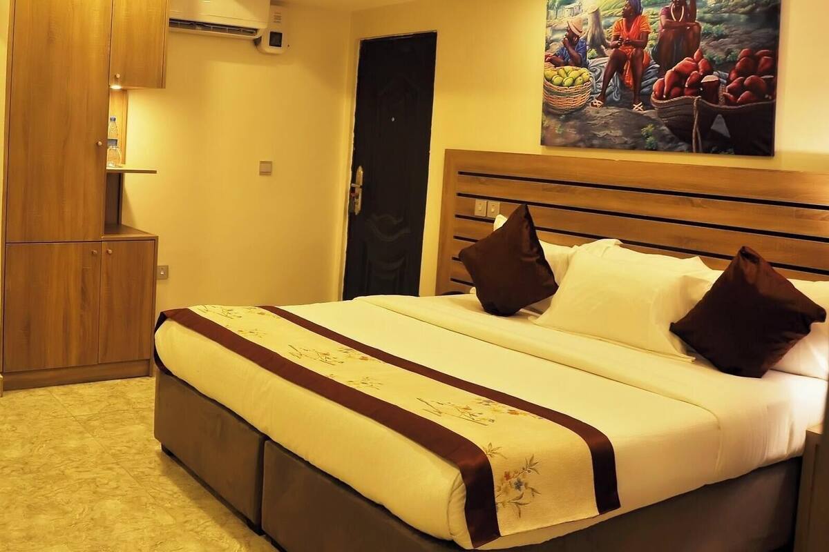 Une chambre d’hôtel avec un lit, un bureau, une armoire et un tableau au mur.