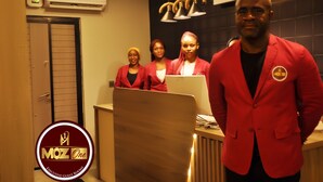 A reception area with a wooden reception desk, a clock on the wall, and an air conditioning unit above. - Moz One Executive Guest Rooms Hombori (Abuja)