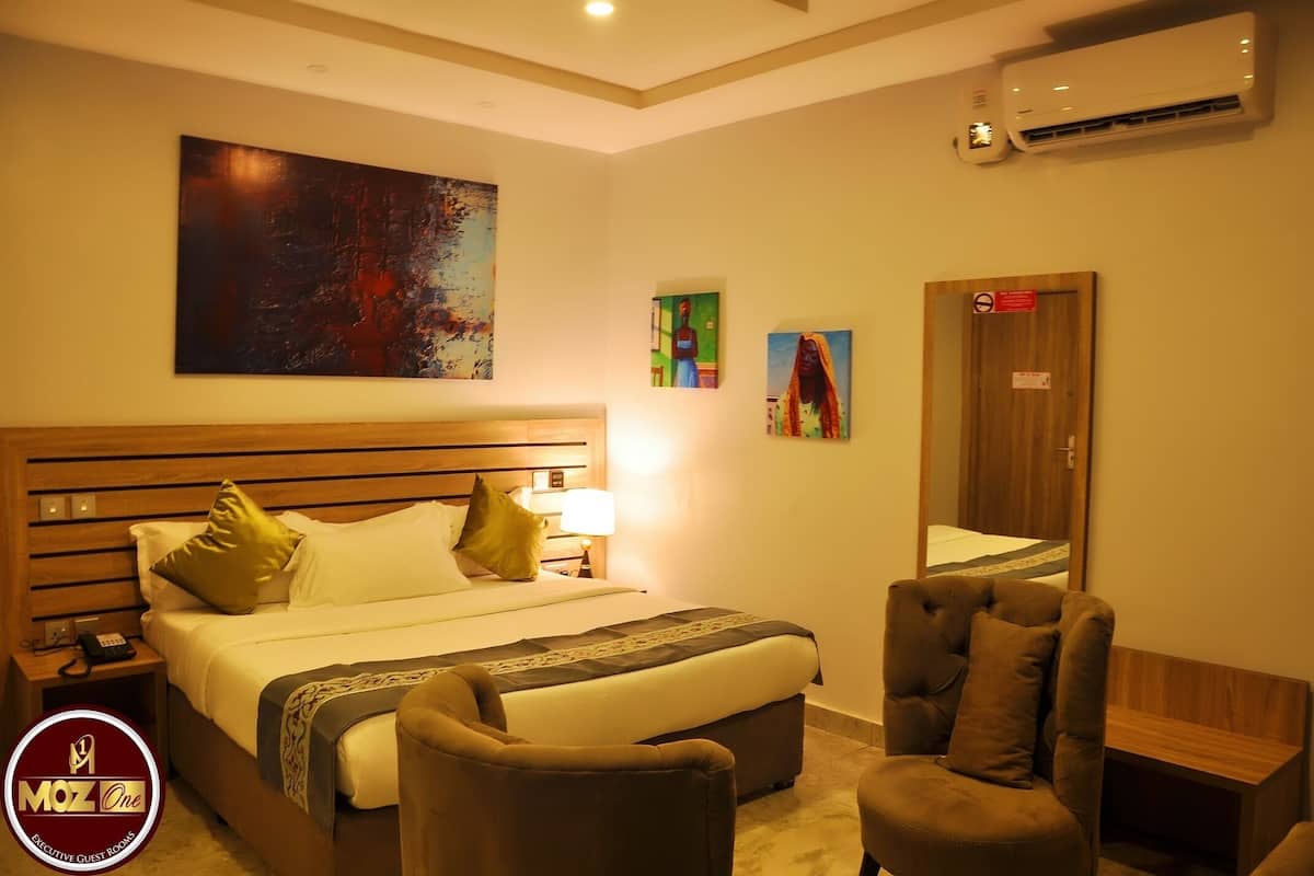Une chambre d’hôtel dotée d’un grand lit, d’un bureau, de deux fauteuils et d’œuvres d’art accrochées aux murs.