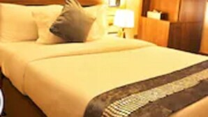 A hotel room with a bed, pillows, a nightstand, a lamp, and a painting on the wall. - Moz One Executive Guest Rooms Hombori (Abuja)