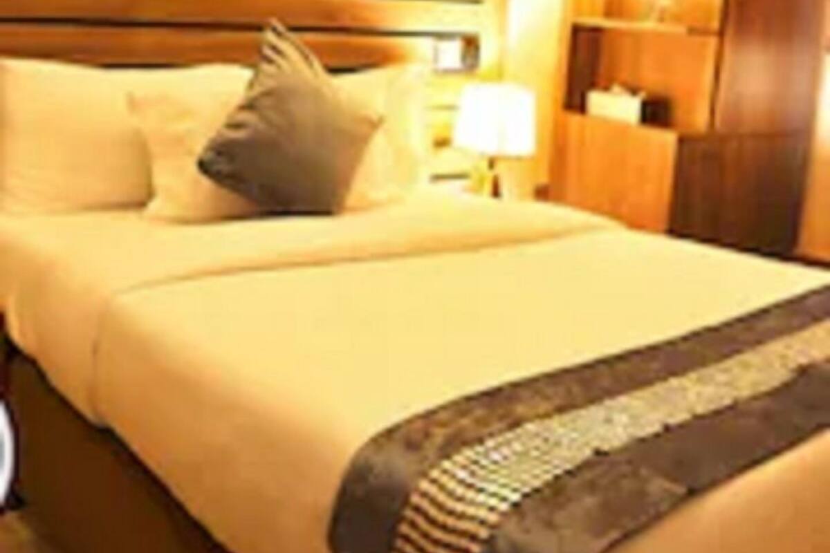 Une chambre d’hôtel avec un lit, des oreillers, une table de chevet, une lampe et un tableau au mur.