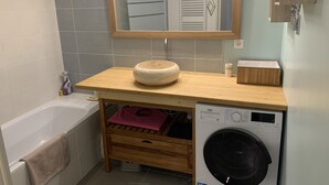 A compact bathroom with a wooden vanity, a sink, a washing machine, and a mirror above the vanity. - Air-conditioned ground-floor apartment with garden (St Cyr sur Mer)