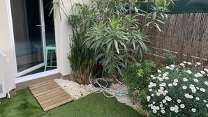 A small garden area with artificial grass, a wooden deck, and a variety of plants including a bamboo fence and flowering plants. - Air-conditioned ground-floor apartment with garden (St Cyr sur Mer)