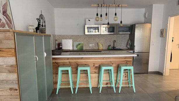 A modern kitchen with a wooden island, bar stools, and stainless steel appliances. - Air-conditioned ground-floor apartment with garden (St Cyr sur Mer)
