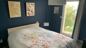 A bedroom with a bed, two wall-mounted paintings, a window with curtains, and a view of greenery outside. - Air-conditioned ground-floor apartment with garden (St Cyr sur Mer)