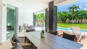 Un espace repas extérieur moderne, avec une longue table, des chaises en osier et une plante en pot.