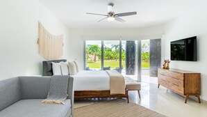 Une chambre à coucher moderne avec un lit, un canapé gris, une commode en bois et un téléviseur.