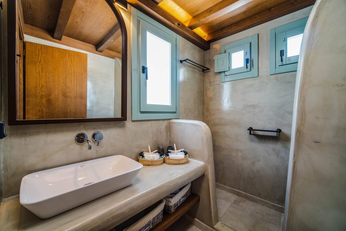 Ein Badezimmer mit einem großen weißen Waschbecken, Holzbalken an der Decke und hellblauen Schränken.