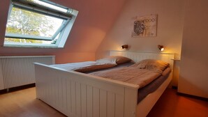 A bedroom with a sloped ceiling, a bed with a white headboard, a window with a view of trees, and a wall-mounted artwork. - Cozy 2 room apartment (List)
