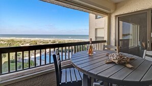 Un balcon avec une table, des chaises, une bouteille de vin et une vue sur la plage et l’océan.