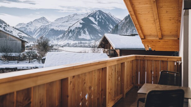 A wooden balcony with a view of snow-covered mountains and a small building in the background.