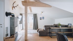 A modern living room with a fireplace, a sofa, a dining table, and a wooden ceiling beam.