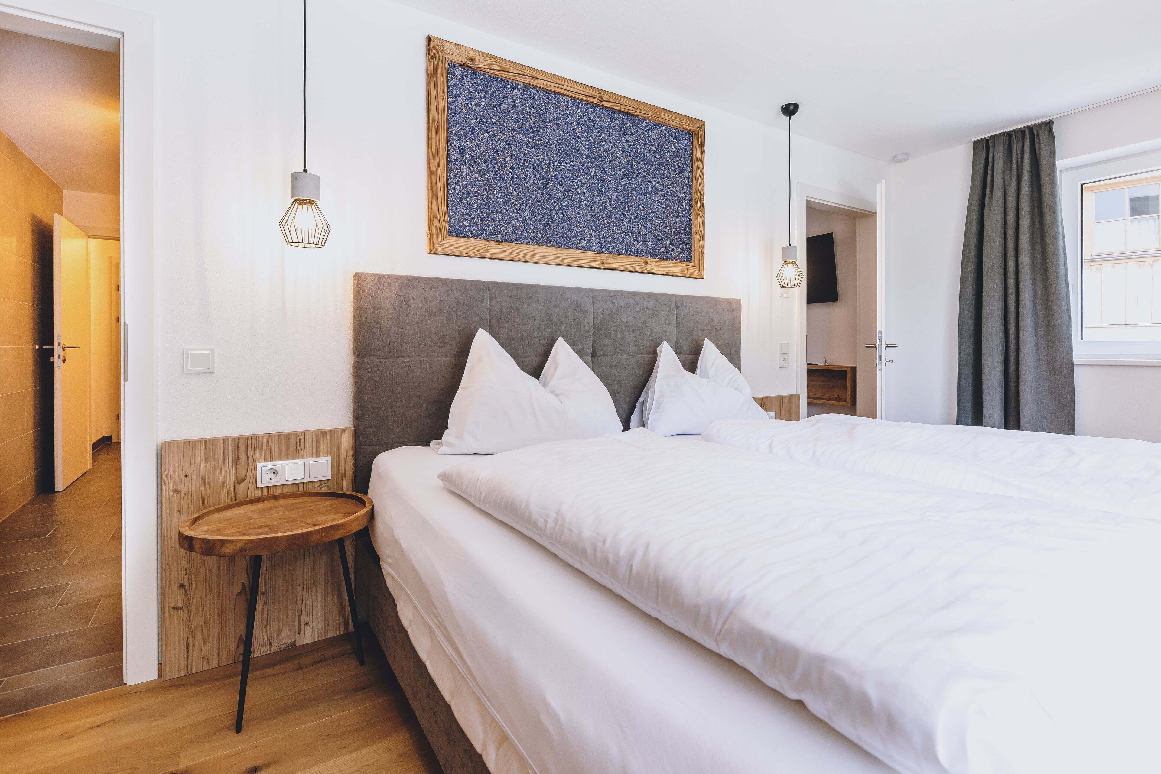 A hotel room with a large bed, a wooden side table, a wall-mounted artwork, and a hanging light fixture.