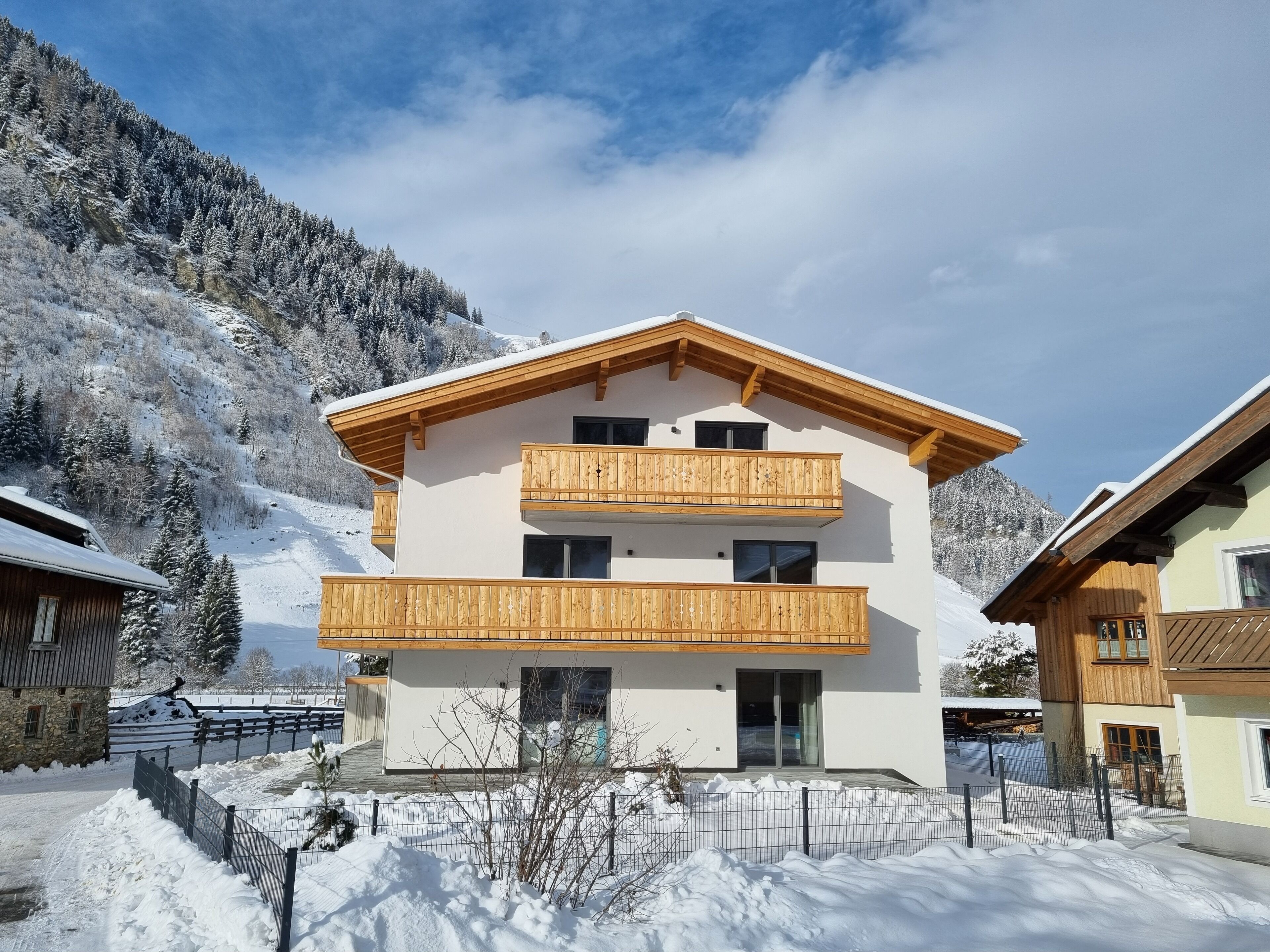 A two-story chalet with wooden balconies, a stone facade, and a view of snow-covered mountains.