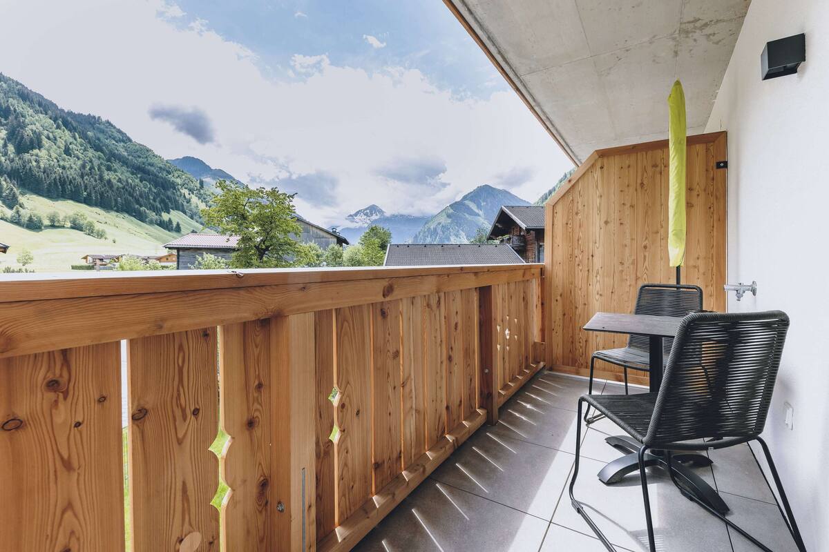 A balcony with a wooden railing, a table, and two chairs.