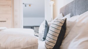 A neatly made bed with white linens and striped pillows, a grey headboard, and a light fixture on the wall.