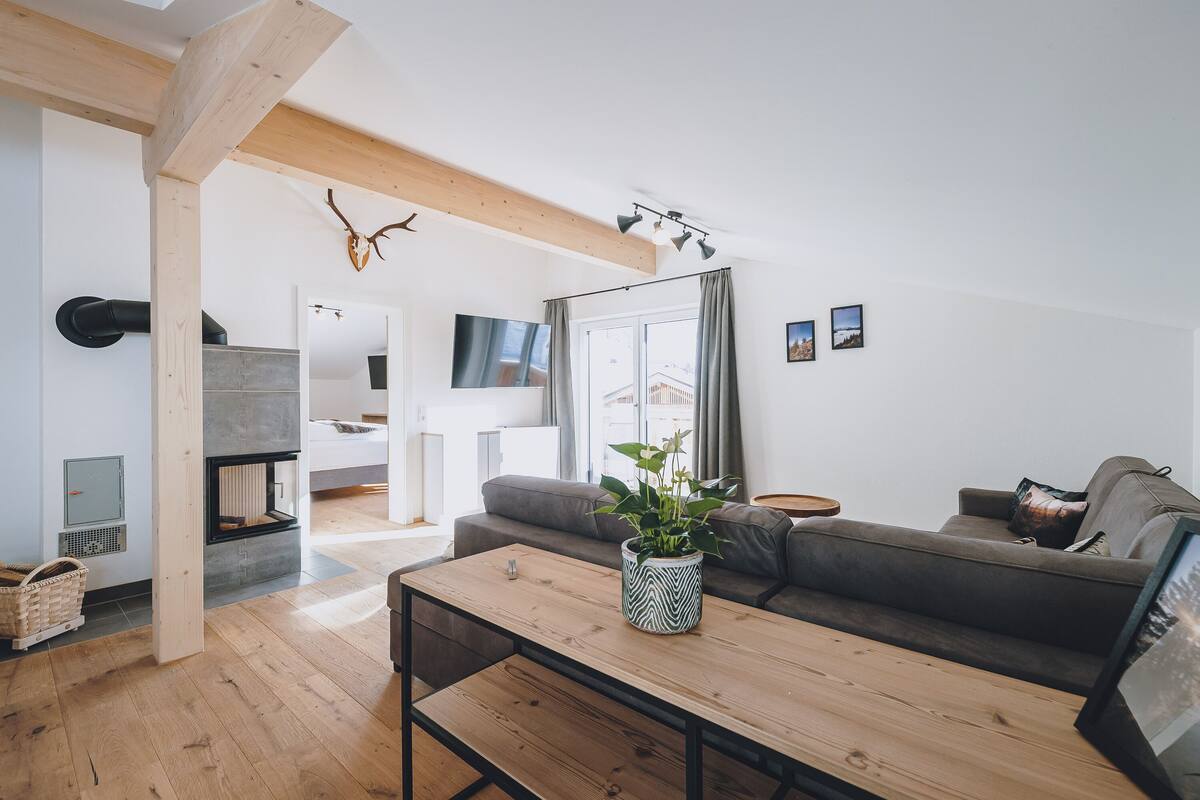 A modern living room with a wooden floor, a grey sofa, a wooden coffee table with a plant, and a fireplace.