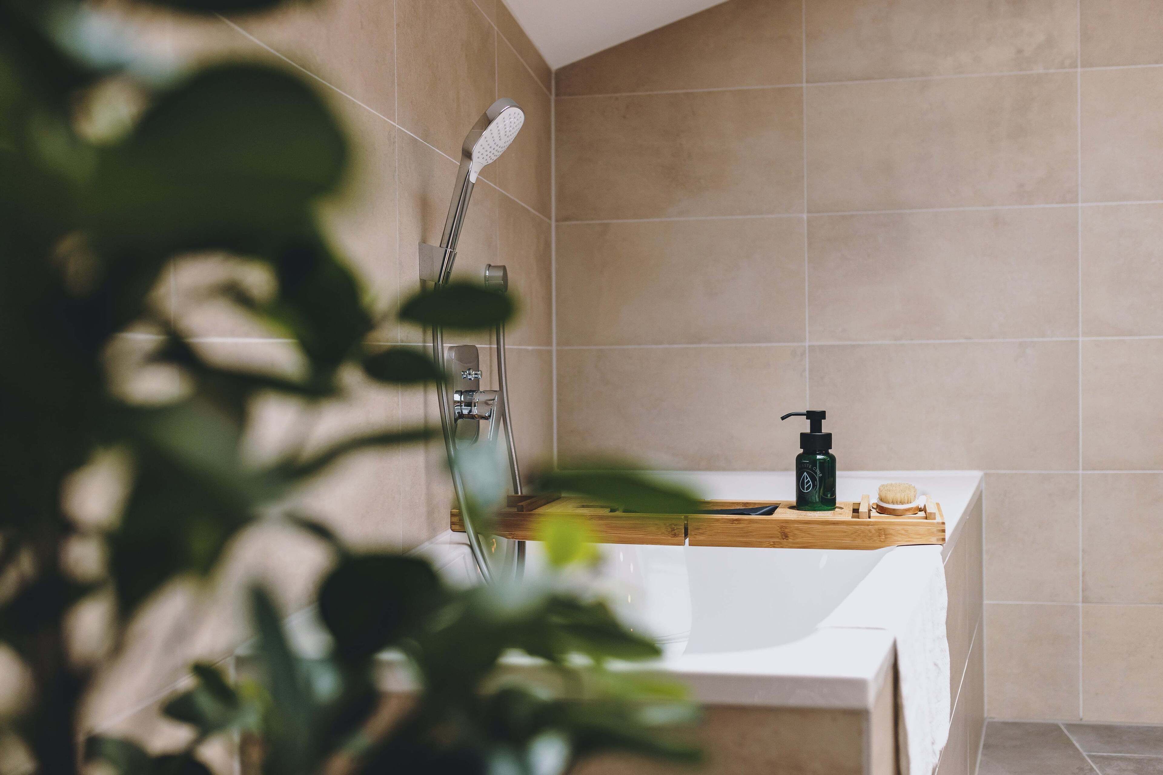 A modern bathroom with a white bathtub, a wooden tray with toiletries, and a handheld showerhead.