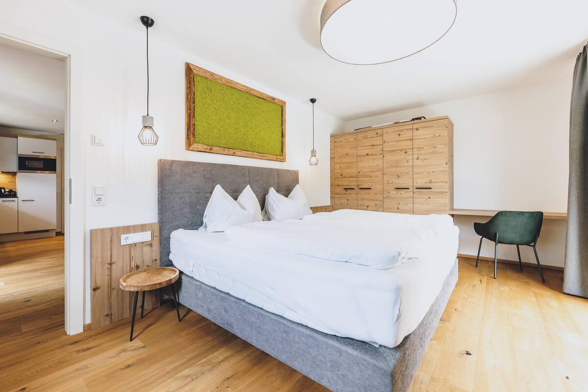 A bedroom with a bed, a wooden wardrobe, a desk, and a chair.