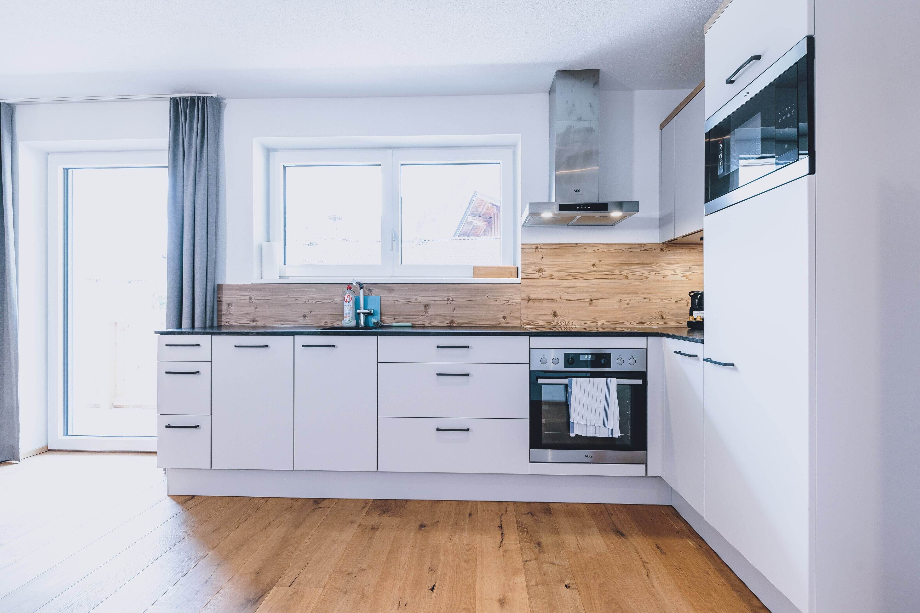 A modern kitchen with white cabinets, a wooden countertop, an oven, and a window with curtains.