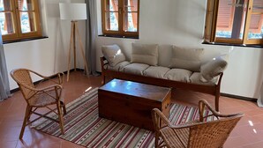 Un salon comprenant un canapé, deux fauteuils en osier, une table basse en bois, un lampadaire et un tapis à rayures.