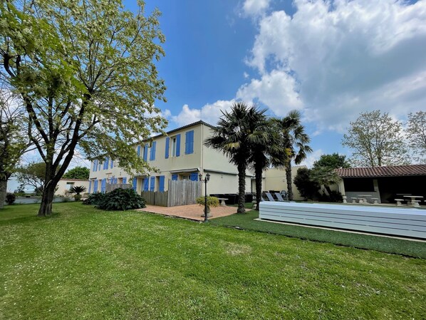 A two-story building with a flat roof, a fenced yard, and a pool area with lounge chairs.