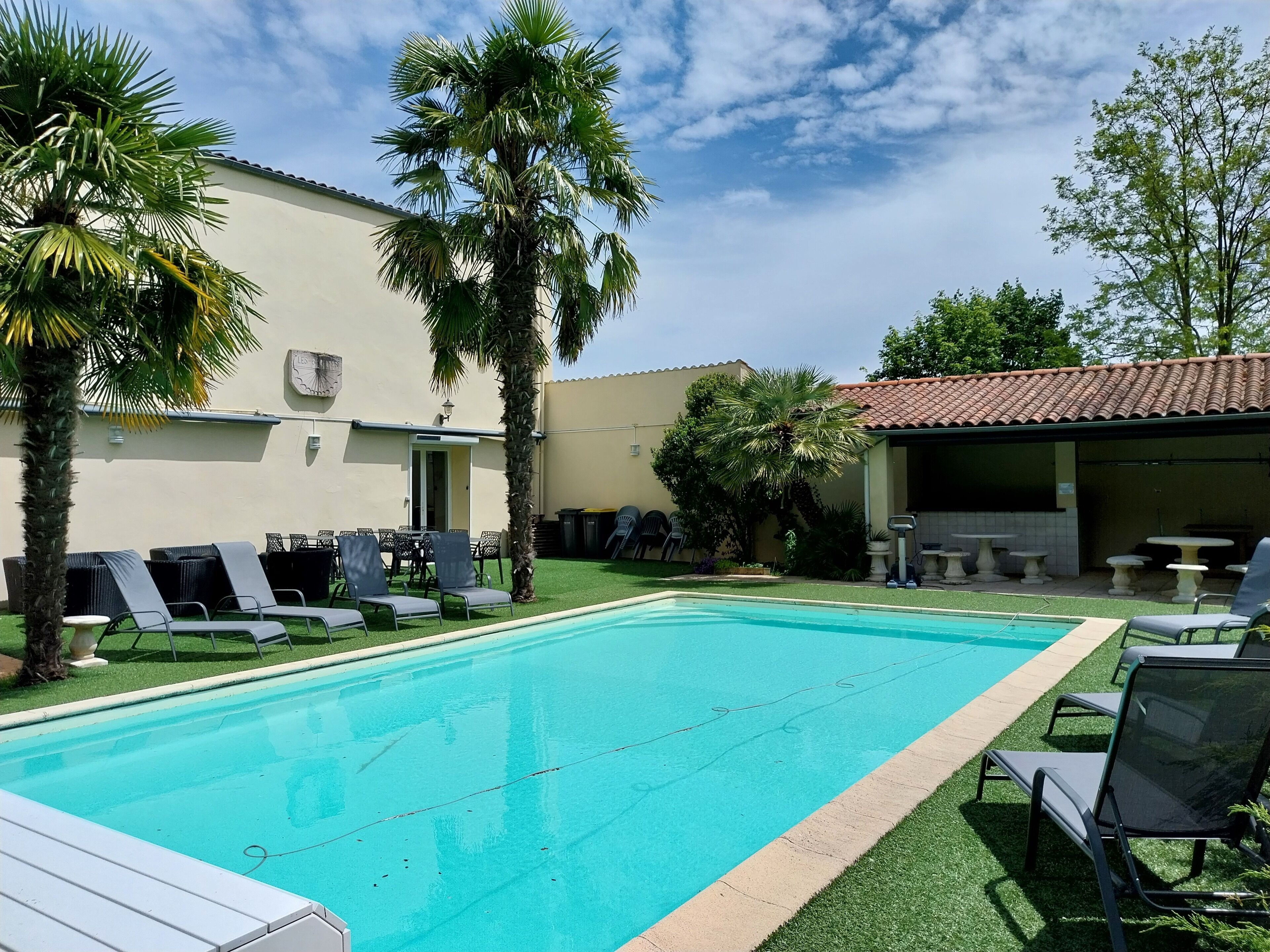 Une piscine avec des chaises longues, des palmiers et un bâtiment doté d’un toit en tuiles.