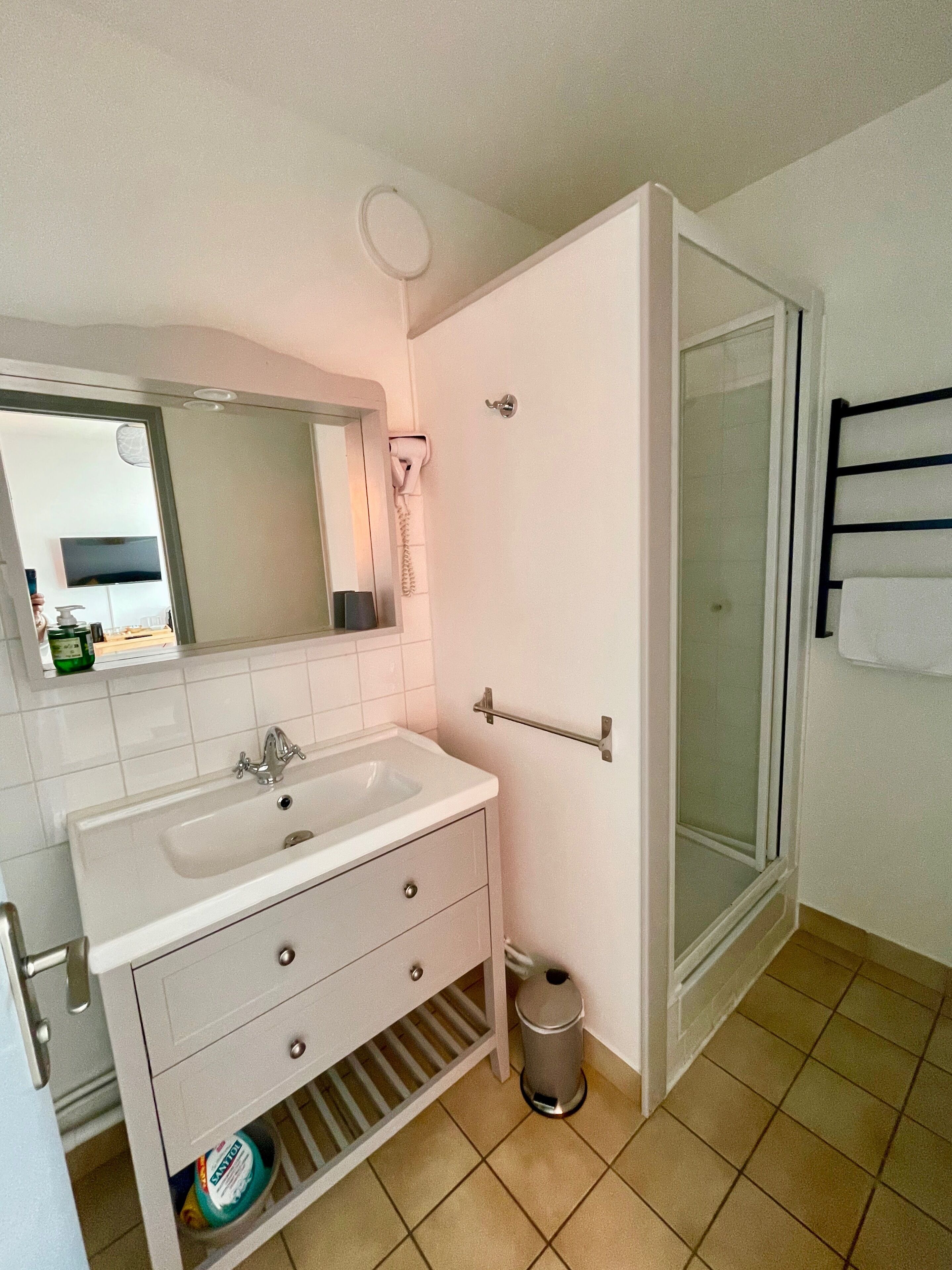 Un baño con lavamanos blanco, espejo y ducha con mampara de vidrio.