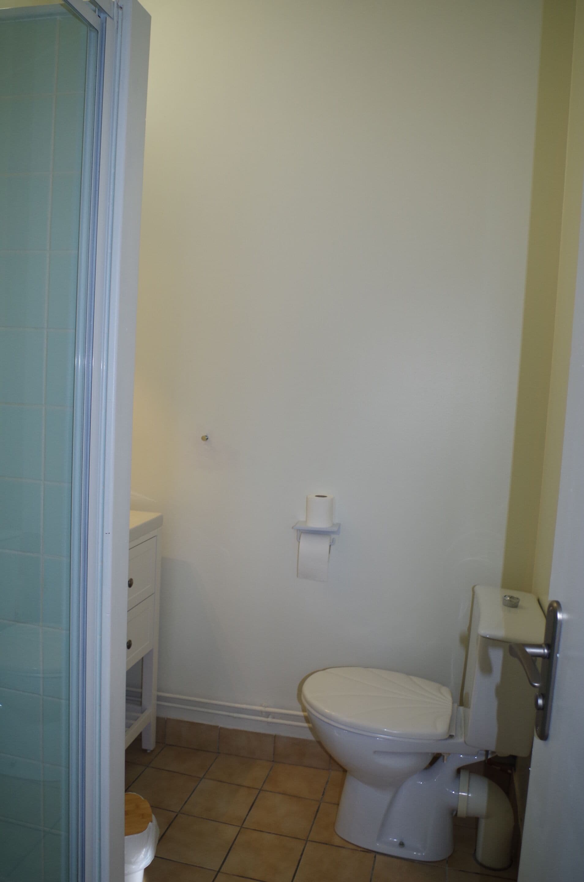 Une salle de bain avec des toilettes, une petite étagère et un porte-rouleau de papier toilette fixé au mur.