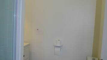 Une salle de bain avec des toilettes, une petite étagère et un porte-rouleau de papier toilette fixé au mur.