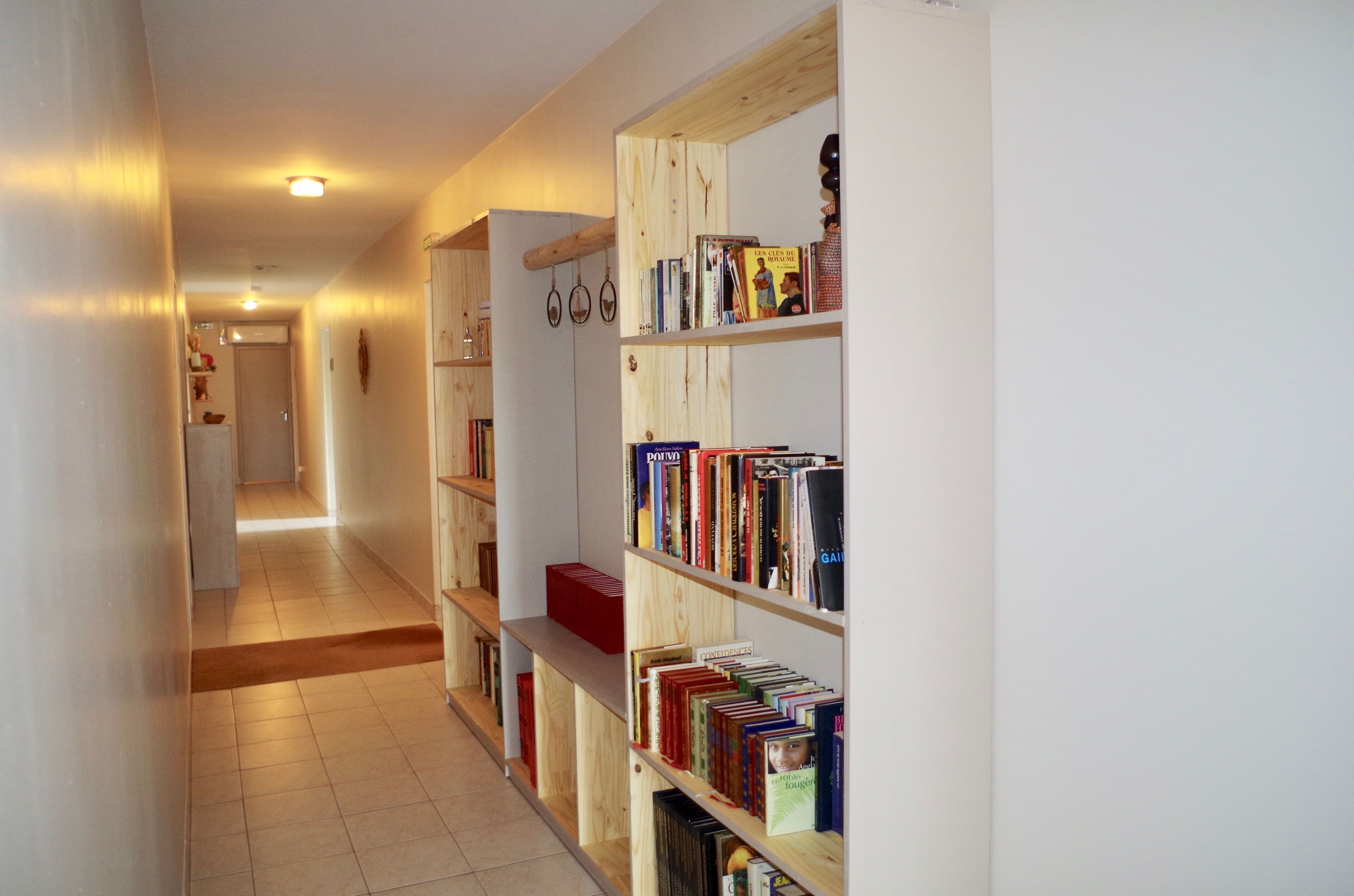 Un couloir avec des étagères en bois remplies de livres, une boîte de rangement rouge et un banc en bois.
