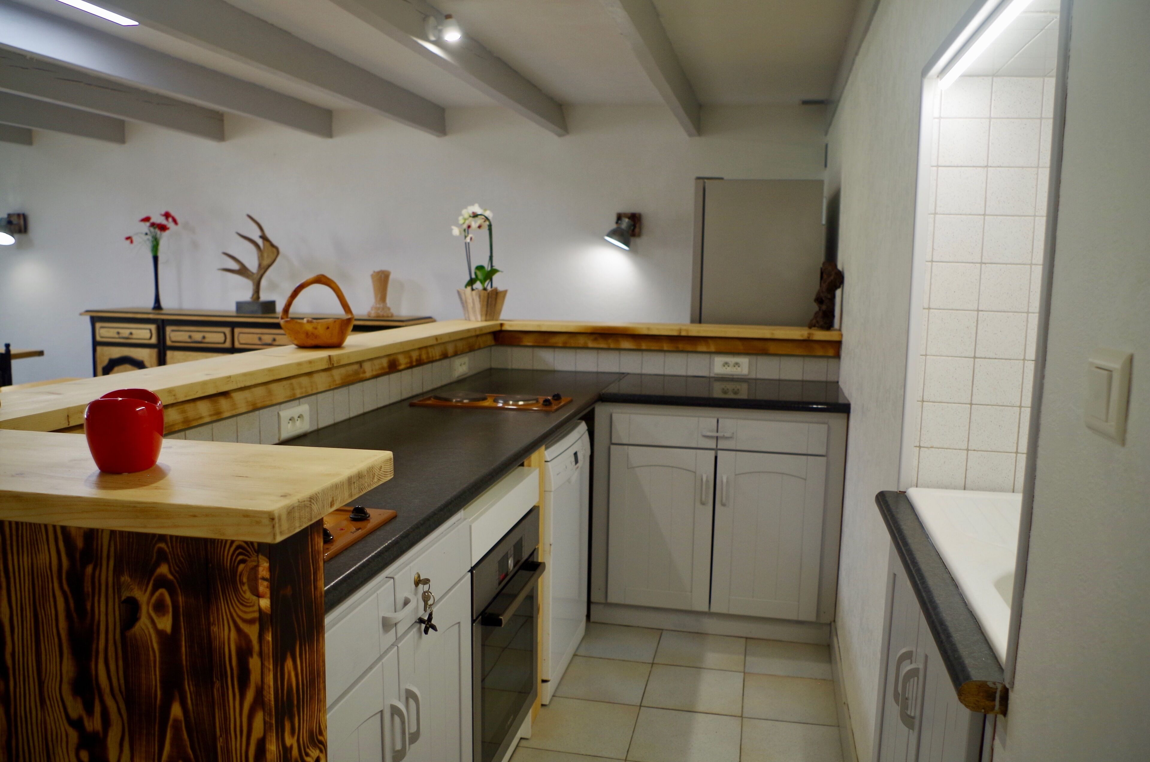 Een keuken met houten aanrecht, witte kastjes, een vaatwasser en een rode mok op het aanrecht.