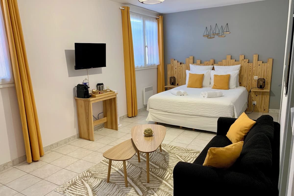 Une chambre d’hôtel moderne équipée d’un lit, d’une table de chevet en bois, d’une télévision, d’un bureau avec une machine à café et d’un canapé.