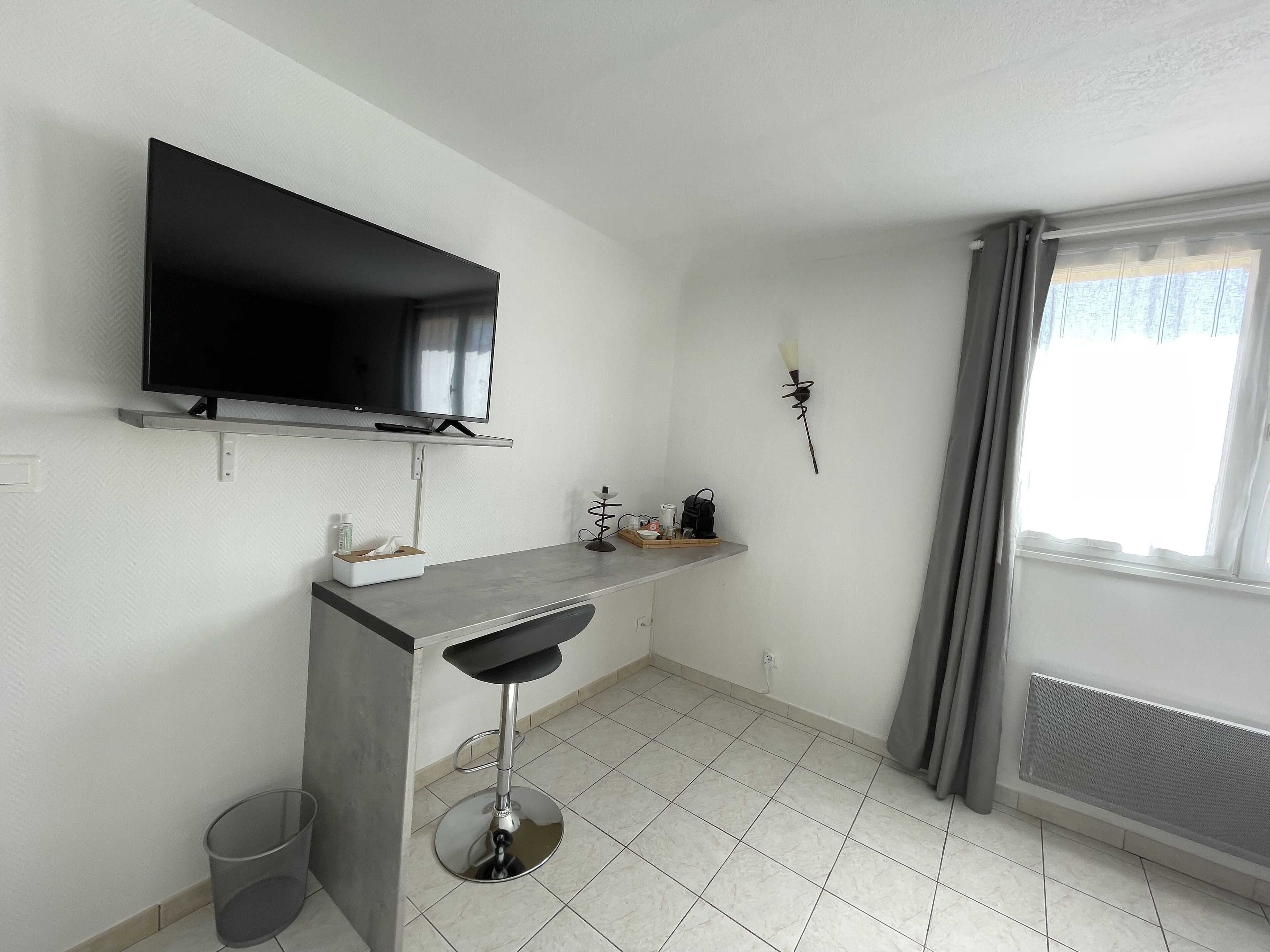 A modern kitchen with a built-in TV, a small bar stool, and a window with curtains.