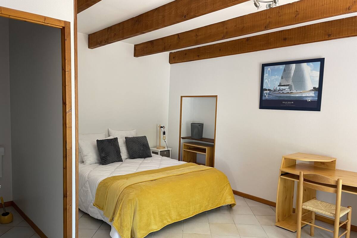 Une chambre à coucher comprenant un lit, une table de chevet, un miroir, un bureau, une chaise et un tableau encadré accroché au mur.
