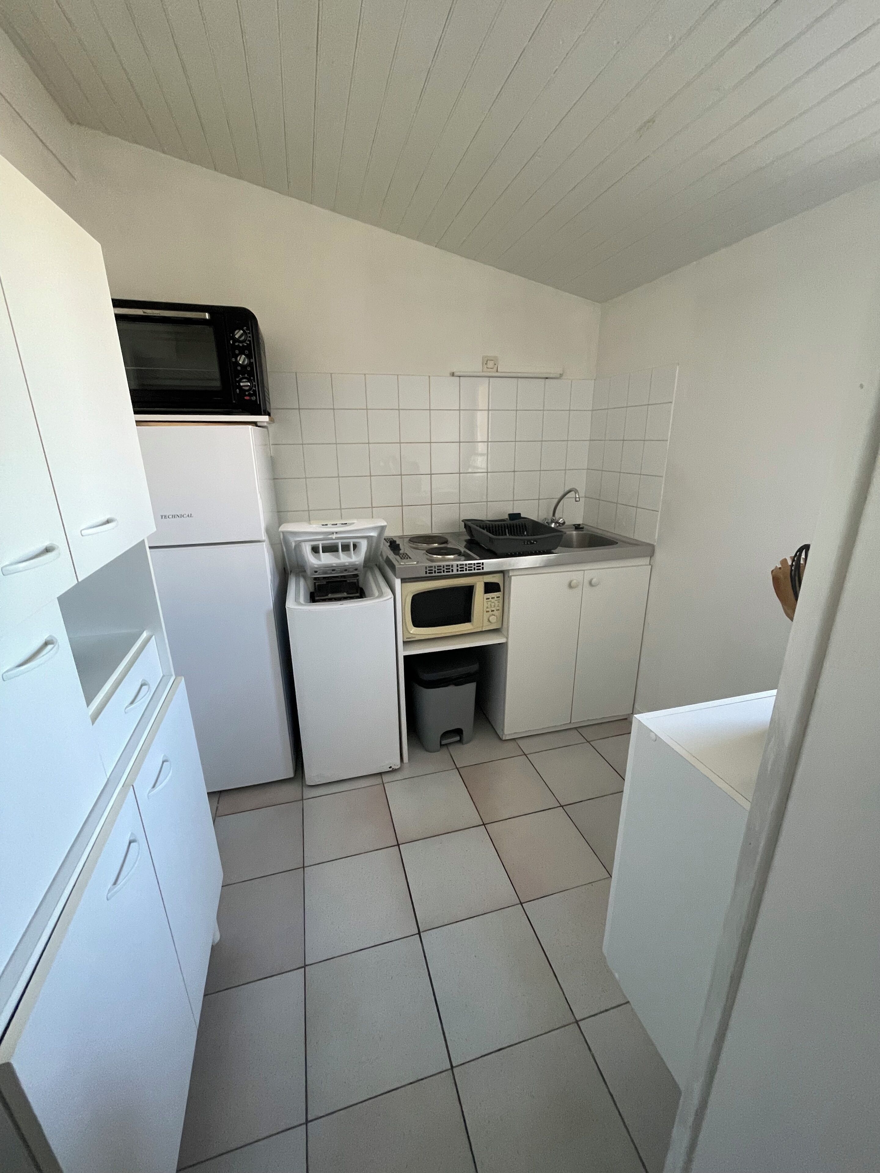 Cocina compacta con gabinetes blancos, microondas, estufa y pileta.