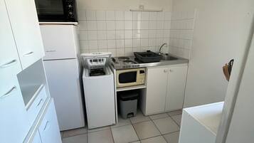 Cocina compacta con gabinetes blancos, microondas, estufa y pileta.