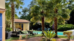A poolside area with lounge chairs, a small building with a tiled roof, and palm trees. - Les Trois Cèdres (Saint Ouen d'Aunis)