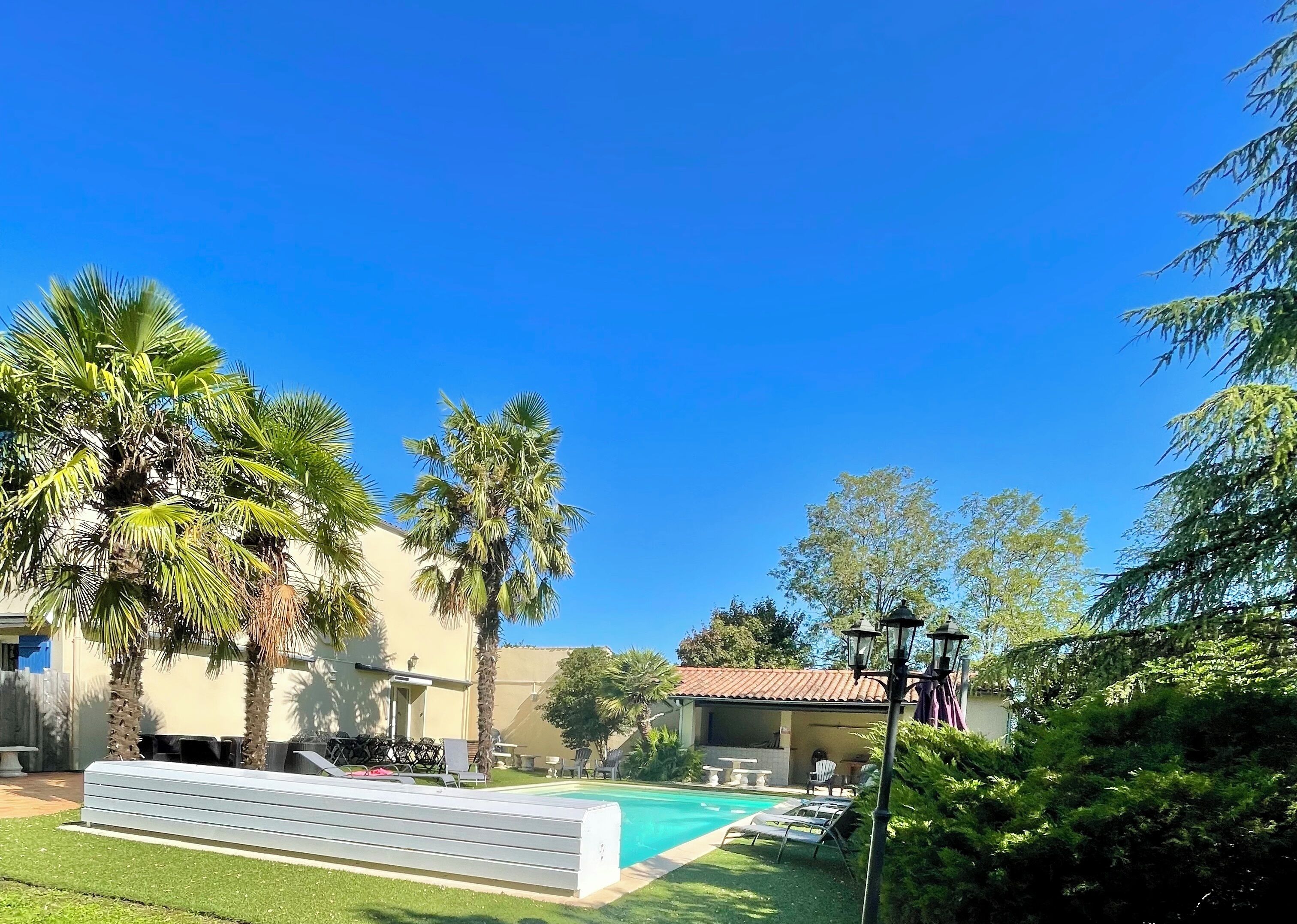 Zona de piscina con sillas de descanso, palmeras y un edificio con tejado de tejas.