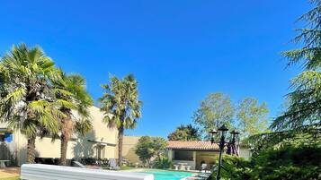 Zona de piscina con sillas de descanso, palmeras y un edificio con tejado de tejas.