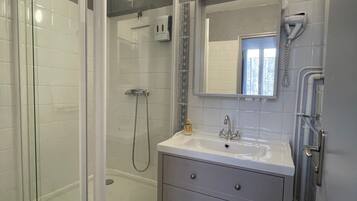 Un baño moderno con ducha de vidrio, tocador con espejo y secador de pelo montado en la pared.