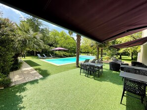 A pool area with artificial grass, lounge chairs, and a covered seating area.
