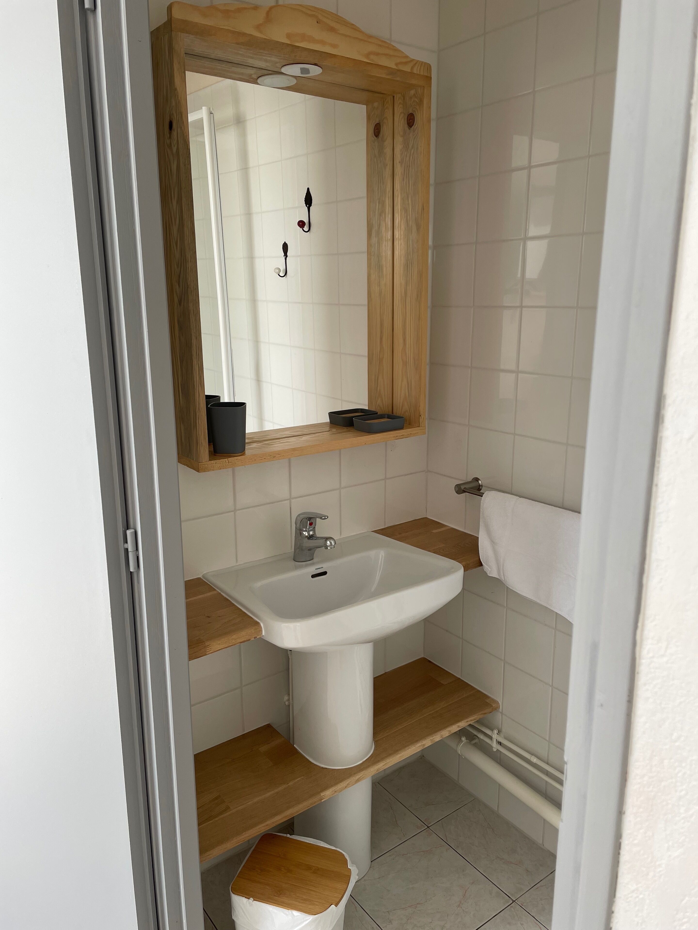 A bathroom with a white sink, wooden shelves, a mirror, and a towel rack.