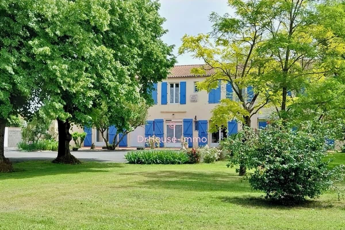 Un bâtiment à deux étages avec des volets bleus, entouré d’une pelouse et d’arbres bien entretenus.