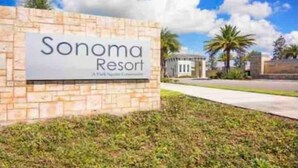 Un panneau indiquant le « Sonoma Resort », avec un mur en pierre et une vue sur des palmiers et un bâtiment en arrière-plan.