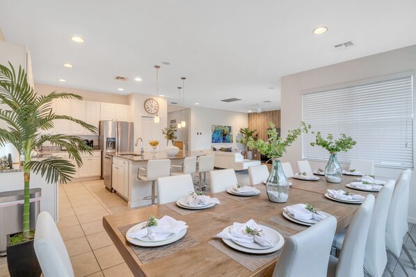 A modern kitchen with white cabinets, a central island, and a dining area with a wooden table set for six.