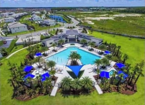 A resort with a central pool, surrounded by palm trees and blue umbrellas.