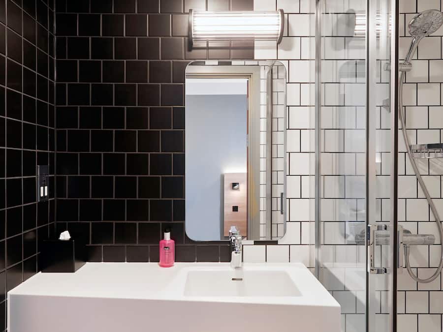 Ein modernes Badezimmer mit einem weißen Waschbecken, schwarzen Fliesenwänden, einer Duschkabine aus Glas und einem Spiegel über dem Waschbecken.