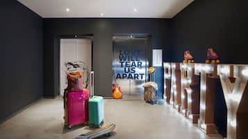 A modern lobby with luggage, a guitar, and a sign that reads "LOVE WILL TEAR US APART".