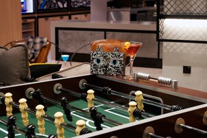 Una mesa de fútbol de mesa con un trofeo decorativo con forma de gato, una copa de cóctel y una butaca de cuero en una habitación moderna con una cocina al fondo.